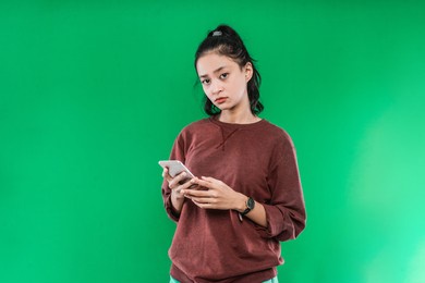 portrait beautiful young asian girl holding a phone while looking at the camera on a green background