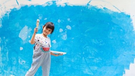 adorable 5 years old asian little girl is smiling while painting the wall with water color at home, concept of art education for kid, homeschooling and learning activity by playing for child.