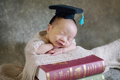 cute clever baby in black graduation cap sleeping on big books with smiling on blur background