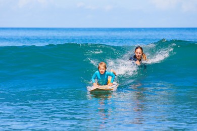 little surf boy - young surfer learn to ride on surfboard with instructor at surfing school. active family lifestyle, kids water sport lessons, swimming activity in summer camp. vacation with child.