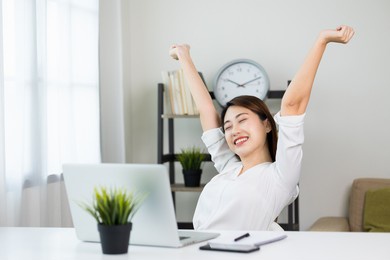 young beautiful asian business woman finish working and celebrate with two hand stretch in the air. women finished work and rest she works at home in the living room.