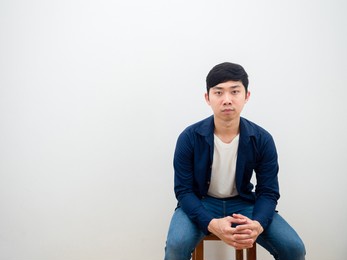 asian man with jeans sitting on chair serious face looking at camera on white isolated background