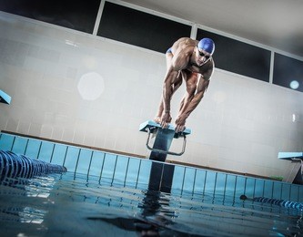 young muscular swimmer in low position on starting block in a swimming pool