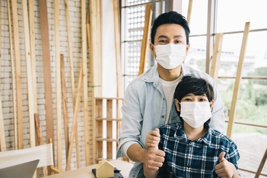 handsome asian carpenter with son wear surgical mask and prepare tools accessories for further refinement within a building or condominium. construction concept. wood store