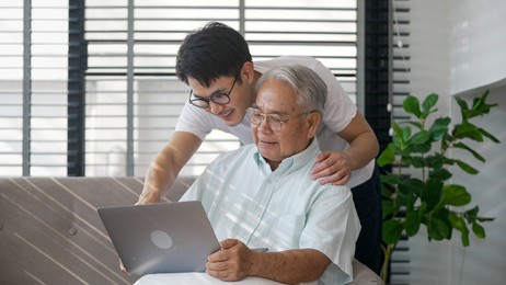 happy two generation asian family son and old man father enjoying happily together using tablet, laptop to watching video and using applications social media.old man with happy life after retired.