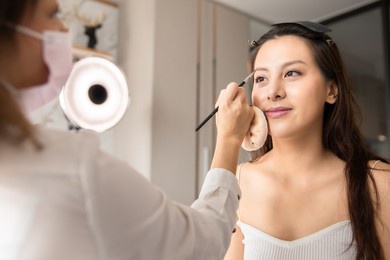 young asian woman in bedroom. make-up artist in beauty studio doing makeup for beautiful girl.beautiful young master make-up artist applies powder brush to face.woman profile making up using pencil.