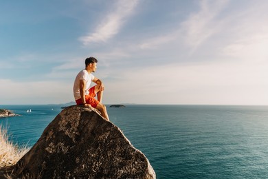 asian man rest on the sea cliff rock after finish his hike trail.