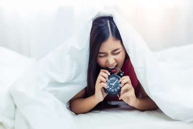 lazy worker woman get frustrated of alarm clock asian girl wake up late in monday morning and she get angry when she wake up so late female will go to work running late she biting alarm clock at bed