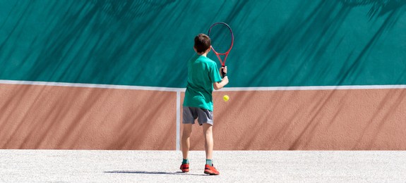 child boy tennis player play tennis alone, practicing hitting technique, training against the wall. sports, games and leisure activities for children outside. back view, wide banner, copy space