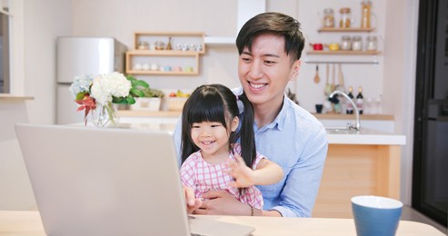 asian young man and his daughter have video chat with computer happily