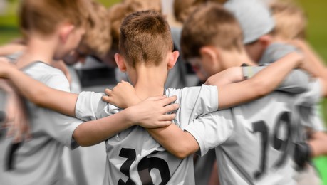 junior sports team celebrating winning. happy kids huddling and standing in team in a circle. boys in white soccer jersey shirts