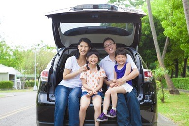 happy family sitting in the car and their house behind