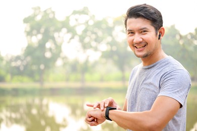 young athletes take a break during exercise in the park and adjust their smart watches. asian men set up their smartwatch before jogging in winter or autumn.