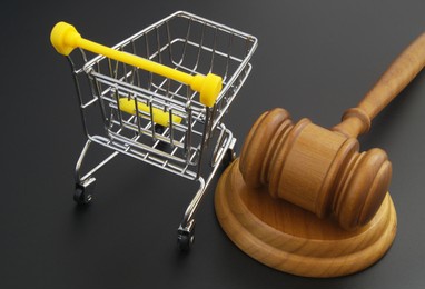 wooden judge gavel and shopping cart on black table. commercial law and consumers rights concept.
