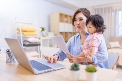 asian business woman works from home by laptop and takes care of her daughter