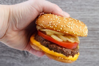 hand holding a burger with fried onion , gray wood background