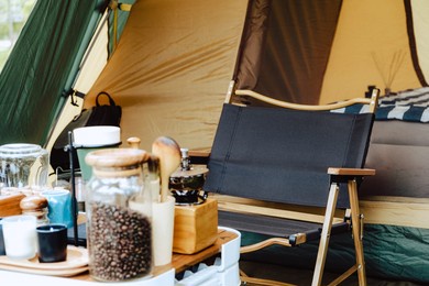 camper picnic tent campground in the outdoor hiking forest. coffee and stove equipment on camping table with chair while campsite in nature background at summer camp. adventure travel vacation concept