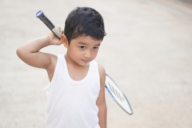 asian boy 3 year old holds a badminton racket and he makes a very happy laughing face outdoor exercise concept.