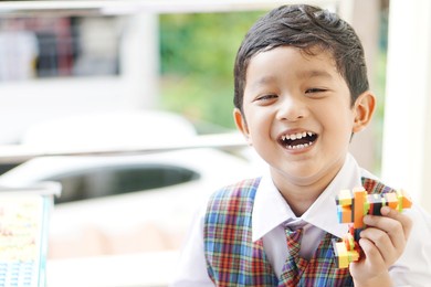 cute asian boy about 3 years old wearing a school uniform is happy to go to school. kid playing lego on the table.                               