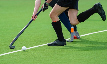 two field hockey player, fighting for the ball on the midfield during an intense match on green grass. professional sport concept
