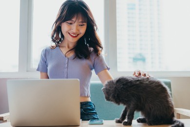 young girl sitting working on sofa and cat sitting next to laptop