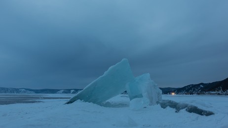 ice hummocks on a frozen and snow-covered lake against a cloudy sky. dusk. a mountain range is visible in the distance. baikal