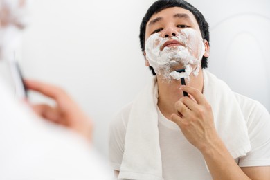 man using razor to shaving his face with cream foam in the bathroom mirror