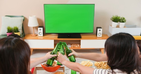 close up of asian young friends making a toast while celebrating some joyful sports moment in living room with green chroma key screen tv