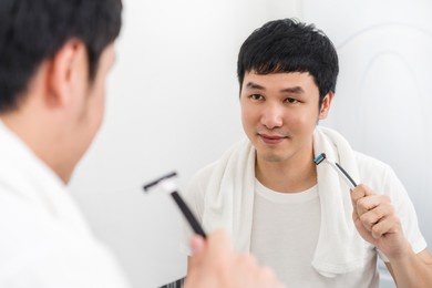 man shaving his face finished and holding razor in the bathroom mirror