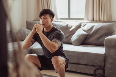 fit man in sportwear doing squat exercise at home. young asian man doing workout at home. home exercise in quarantine.