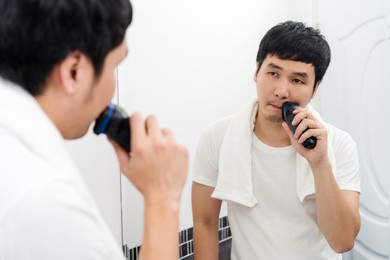 man using electric shave to shaving his face in the bathroom mirror