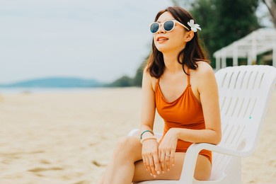 a cute asian woman in an orange swimsuit is sitting on a beach chair sunbathing. she was relaxed on vacation during the summer. summer concept.