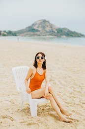 a cute asian woman in an orange swimsuit is sitting on a beach chair sunbathing. she was relaxed on vacation during the summer.