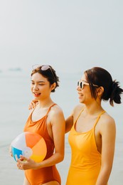 two beautiful asian women wearing orange and yellow bathing suits. they are enjoying on the beach. they feel happy about the summer vacation. summer and friendship concept.