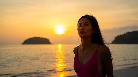 portrait of attractive asian woman in swimwear holding surfboard and walking on tropical beach at summer sunset. confidence female relax and enjoy outdoor activity lifestyle and extreme sports surfing