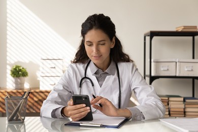 consulting patient by internet. focused female medic sit at workplace hold phone text message to client check health status on distance. woman doctor work with smartphone read email from sick person
