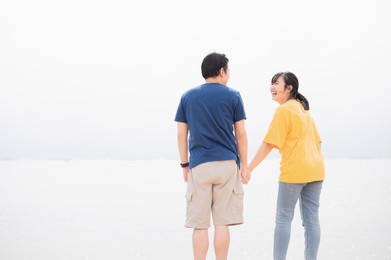 asian couples holding hands together on a private beach by the sea background. happy man and woman laughing together on travel vacation. love affection and valentines day concept. copy space