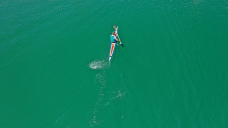 aerial drone top down photo of young athlete rowing in emerald lake