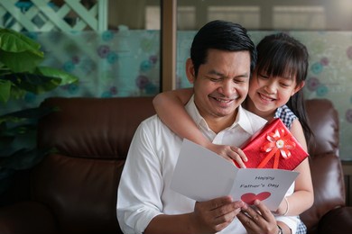 asian little child daughters congratulating dad and giving him postcard and gift box with smiling and hugging.concept of happy father's day
