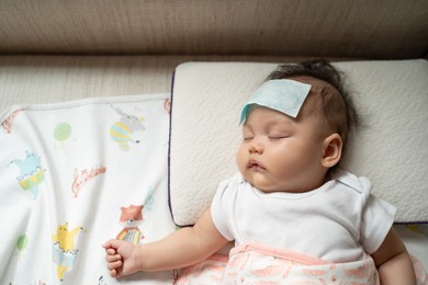 asian baby infant get fever and apply cool patch on forehead sleeping at home after vaccination. cold pad gel healing temperature. baby sick after back from hospital.