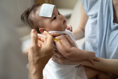 asian baby infant get fever and apply cool patch on forehead getting injection for vaccination on arm by doctor. cold pad gel healing temperature. baby sick and crying.