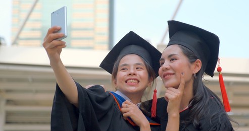 young asian women in graduation gown outfit meeting outdoor and take a selfie together with smile and happiness in university graduate event. celebrating graduation from university.