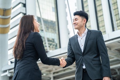 asian businessman and woman handshake in the city with highrise building in background. partnership agreement successful after complete the negotiation. business deal, merger and acquisition concepts.