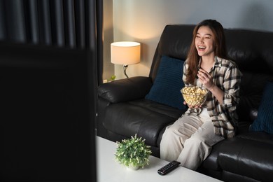funny young woman watching tv and eating popcorn on sofa at night