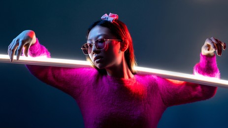 cyberpunk fashion. neon light people. futuristic portrait. glamour asian girl in pink in sunglasses in red color glow with illuminated white led lamp stick isolated on dark night blue.