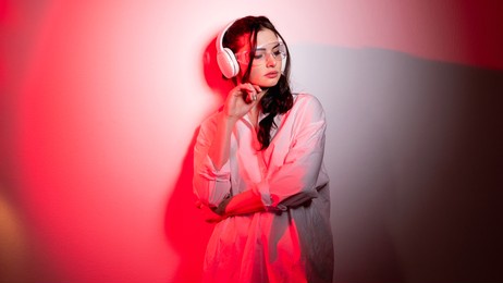cyberpunk music. neon portrait. youth lifestyle. digital technology. relaxed girl in wireless headphones futuristic glasses in red light on pink color gradient empty space background.