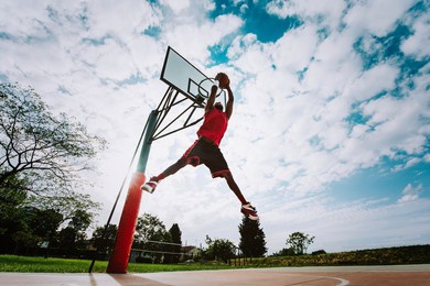 street basketball player making a powerful slam dunk on the court - athletic male training outdoor at sunset - sport and competition concept