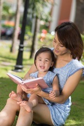 chinese little girl and her mother reading a book in the park