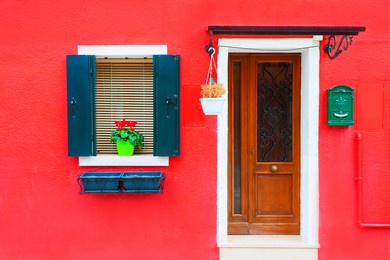 door and window with flower on the red facade of the house. colorful architecture in burano island, venice, italy.