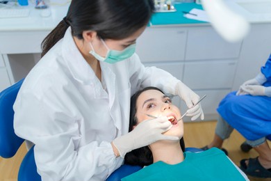 asian female dentist examining young girl patient's teeth at dental clinic. doctor probing teeth with dental instrument using an explorer look for cavities treatment and checking problems with filling